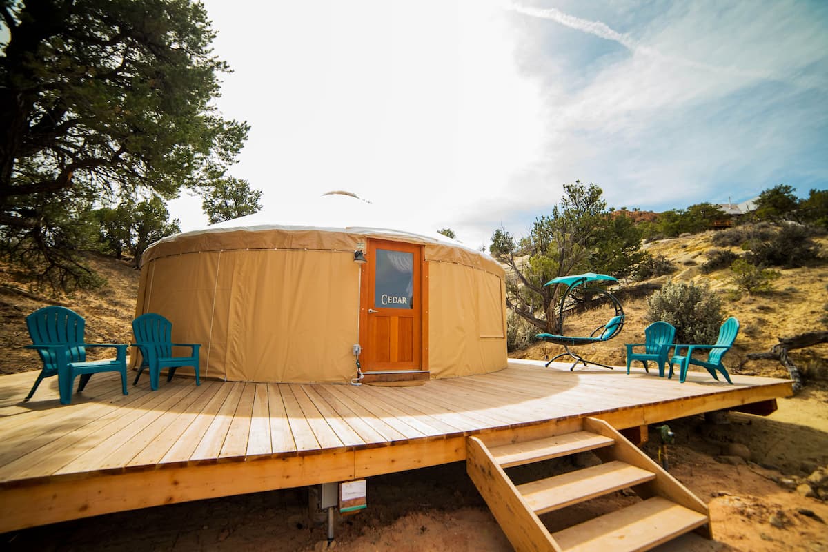 A yurt with a wooden deck, a door labeled "CEDAR," and four turquoise chairs.
