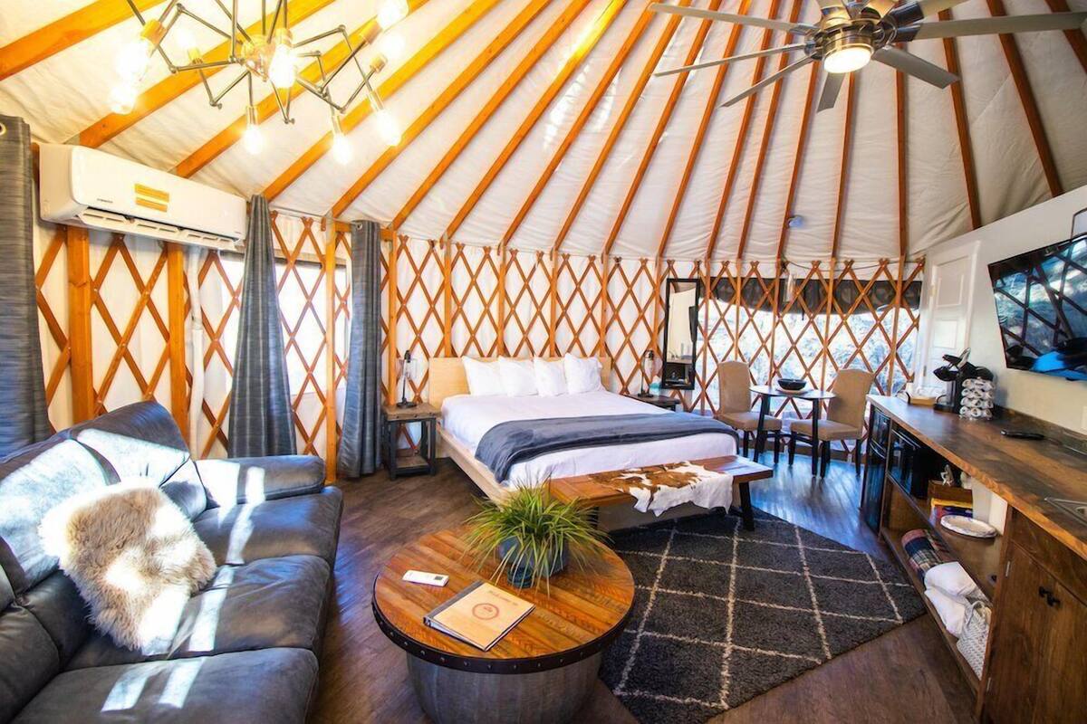 A cozy interior of a yurt with a bed, sofa, dining table, and a TV.