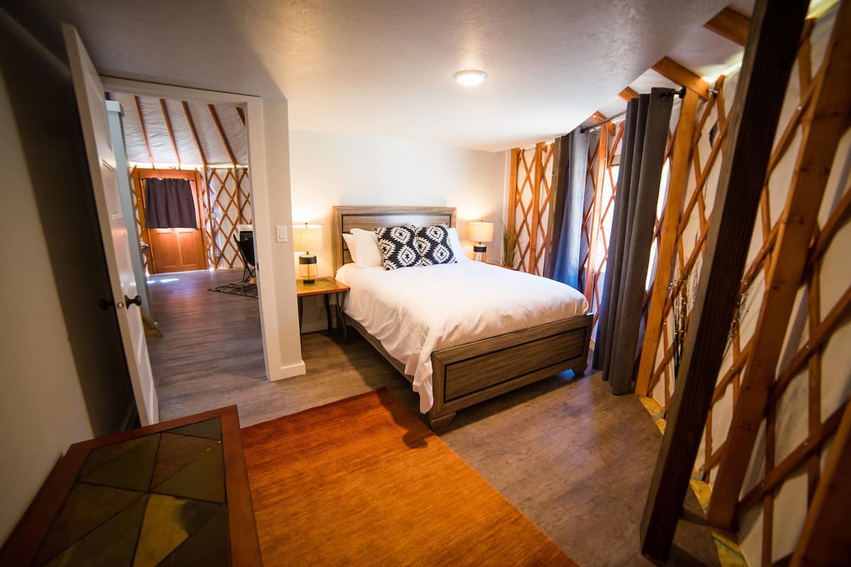 A bedroom with a wooden bed, two bedside tables with lamps, a wooden floor, and a view through a lattice window.