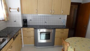 Una cocina con gabinetes color beige, un horno de acero inoxidable, un salpicadero de azulejos y un comedor con mesa y sillas.