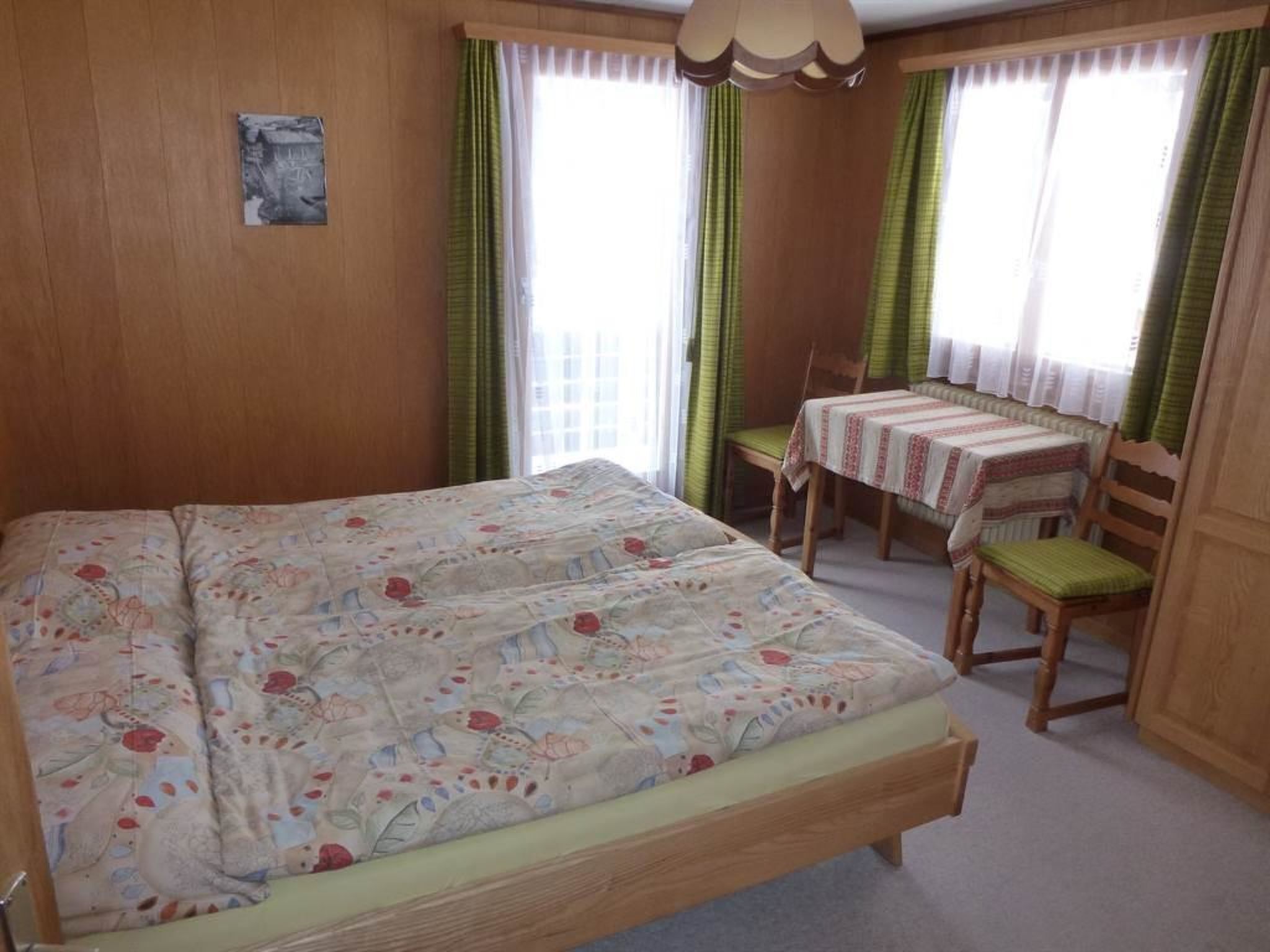 A bedroom with a large bed, a small table with chairs, and a window with curtains.