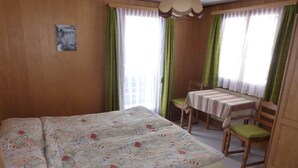 Un dormitorio con una cama grande, una mesita con sillas y un ventanal con cortinas.