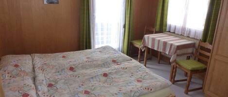 A bedroom with a large bed, a small table with chairs, and a window with curtains.