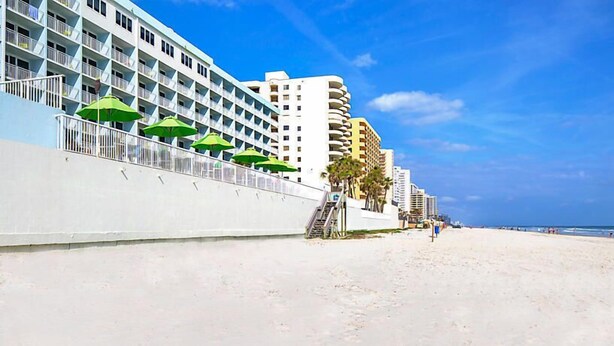 A beachfront hotel with balconies, a sandy beach, and a clear blue sky. - Beach Resort with Ocean Front Pool and Hot Tub (Daytona Beach)