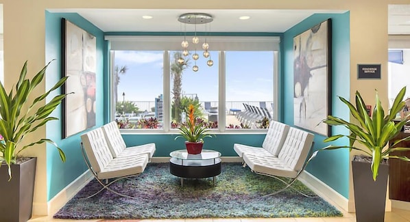 A modern lobby with two white armchairs, a round coffee table, and a large window with a view of palm trees and buildings.