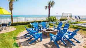 A beachside patio with blue Adirondack chairs, a fire pit, and a yellow umbrella. - Beach Resort with Ocean Front Pool and Hot Tub (Daytona Beach)