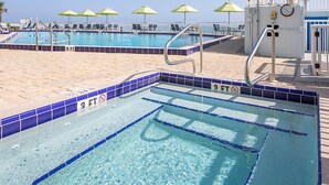 A swimming pool with a 3 FT depth marker, lounge chairs, and umbrellas. - Beach Resort with Ocean Front Pool and Hot Tub (Daytona Beach)