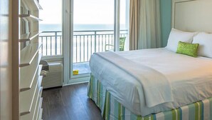 A hotel room with a bed, a window with a view of the sea, a chair, and a dresser. - Beach Resort with Ocean Front Pool and Hot Tub (Daytona Beach)