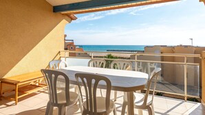 Un balcón con mesa y sillas, con vista a una playa y al mar.