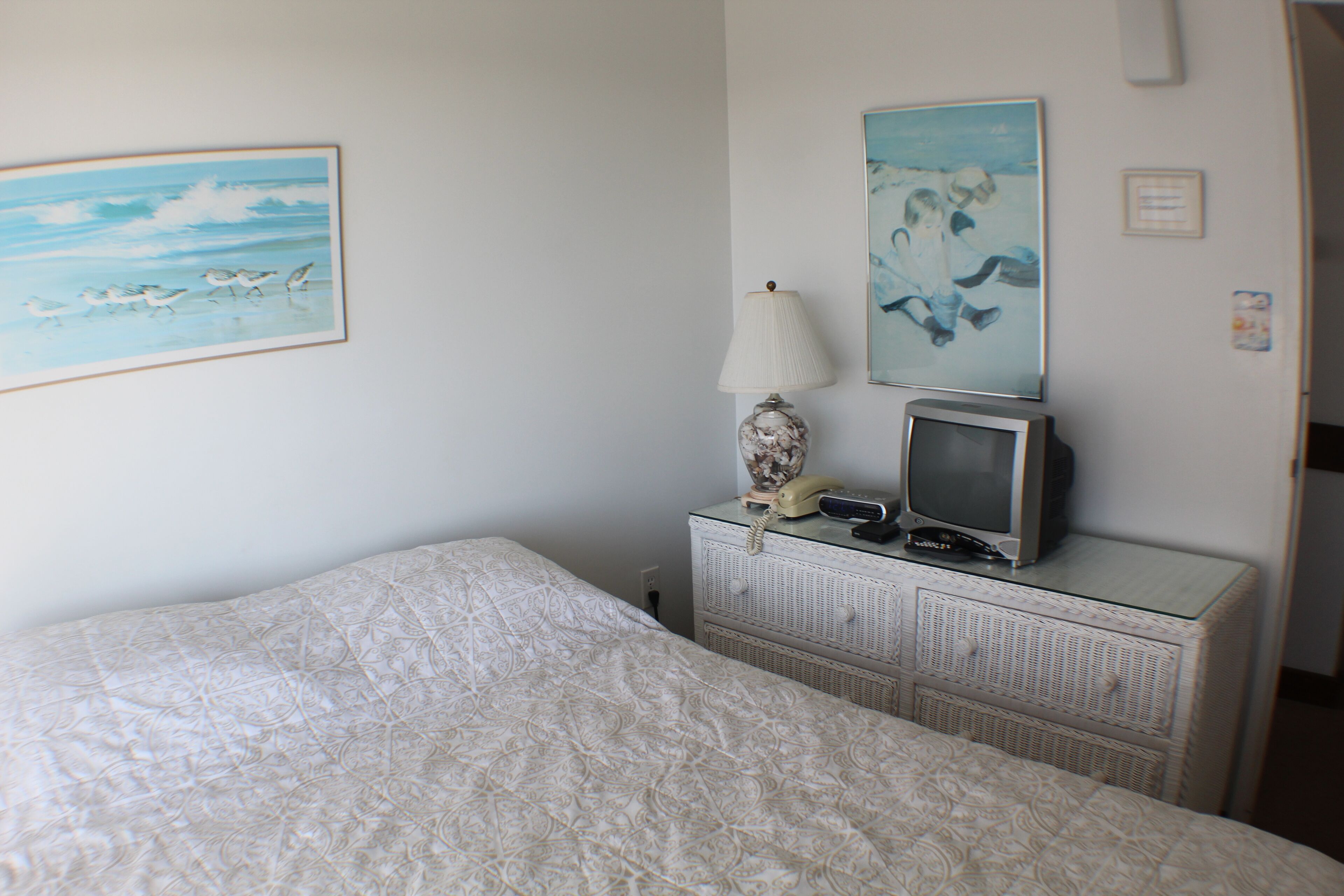 Una camera da letto con un letto, una cassettiera con televisione e lampada, e due quadri appesi al muro.