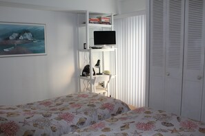 Ein Schlafzimmer mit einem Bett, einem Fernseher auf einem Regal, einem Schreibtisch und einem Kleiderschrank.