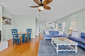 A spacious living room with a blue sofa, a dining table with blue chairs, and a ceiling fan.
