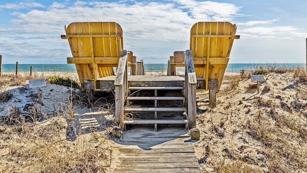 A wooden staircase leading to beach chairs on a sandy beach with a clear sky. - Oceanfront duplex with direct beach access (Emerald Isle)
