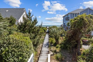 A wooden boardwalk leading to a house with a view of the ocean.