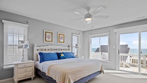 A bedroom with a bed, a nightstand, a ceiling fan, and a view of the beach through the door. - Oceanfront duplex with direct beach access (Emerald Isle)