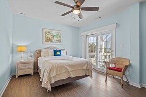 A bedroom with a bed, a nightstand, a chair, a ceiling fan, and a window with a view.