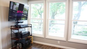 A room with a TV on a stand, a wooden entertainment unit, and large windows with a view of trees.
