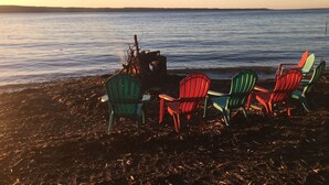 A beach with chairs and a fire pit.