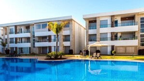 Ett modernt hotell med en swimmingpool, flera balkonger och en välskött gräsmatta.