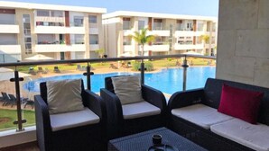 En balkong med möbler i rotting, en pool och utsikt över en hotellbyggnad.