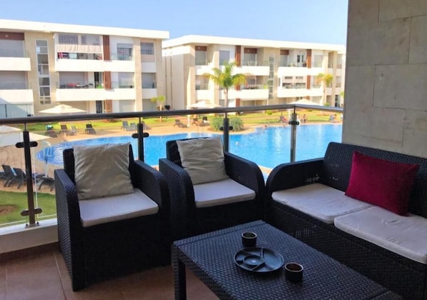 Ein Balkon mit Korbmöbeln, ein Pool und Blick auf ein Hotelgebäude.