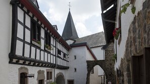 Um estreito beco de paraleipípedos com edifícios tradicionais em enxaimel, uma torre de igreja e muros de pedra.