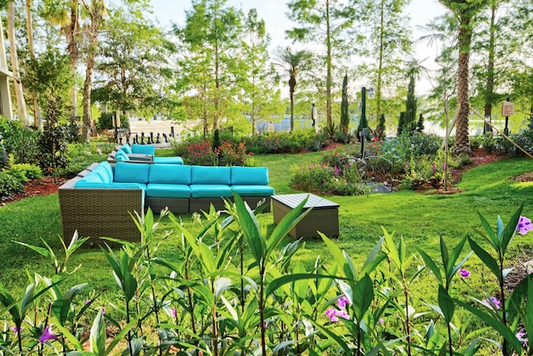 A garden with a blue sofa and wicker furniture, surrounded by lush greenery and flowers.