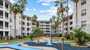 A multi-story hotel with balconies, palm trees, and a children's play area with a shark-shaped slide.