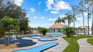 A golf course with a thatched-roof pavilion, a water feature, and a sculpture of a shark.