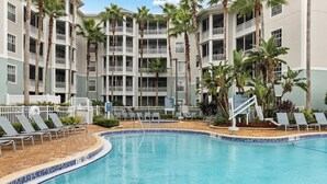 A hotel with a pool, palm trees, and a multi-story building with balconies.