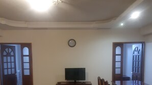 Een woonkamer met televisie, bank, poef en een eettafel met stoelen.