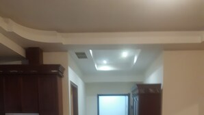 Een ruime hal met een keukenhoek links, een deur naar een andere kamer rechts, en een heldere plafondlamp.