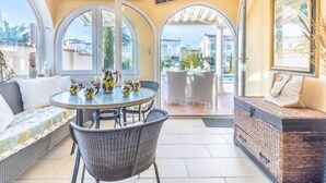 A sunlit patio with a round table, chairs, and a cushioned bench. - Vacation home Bonica by Interhome (Empuriabrava)