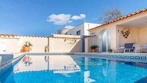 A clear blue swimming pool with a tiled edge, a white building with a tiled roof, and a few potted plants. - Vacation home Bonica by Interhome (Empuriabrava)