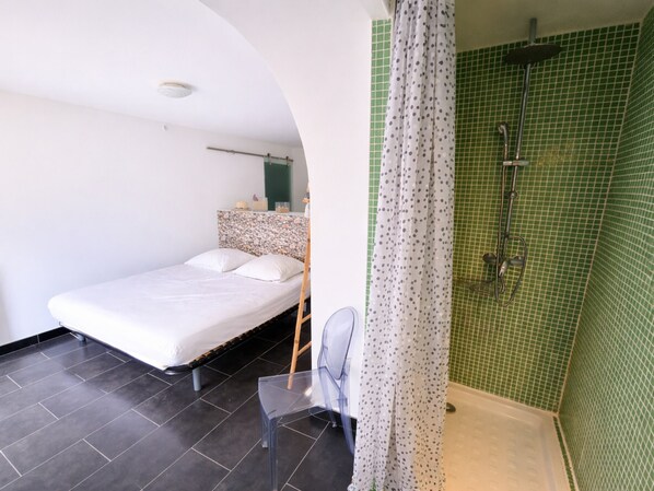 A small, modern room with a bed, a chair, and a shower area with green tiles. - Apartment in Collioure center with terrace & WiFi (Collioure)