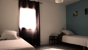 A room with two beds, a window with curtains, a small table, and a hanging light fixture. - New residence, Le Manaka, Turquoise, calm and rest (Lamalou-les-Bains)