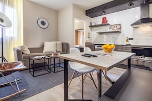 A modern living room with a sofa, coffee table, and a dining area with a table and chairs.