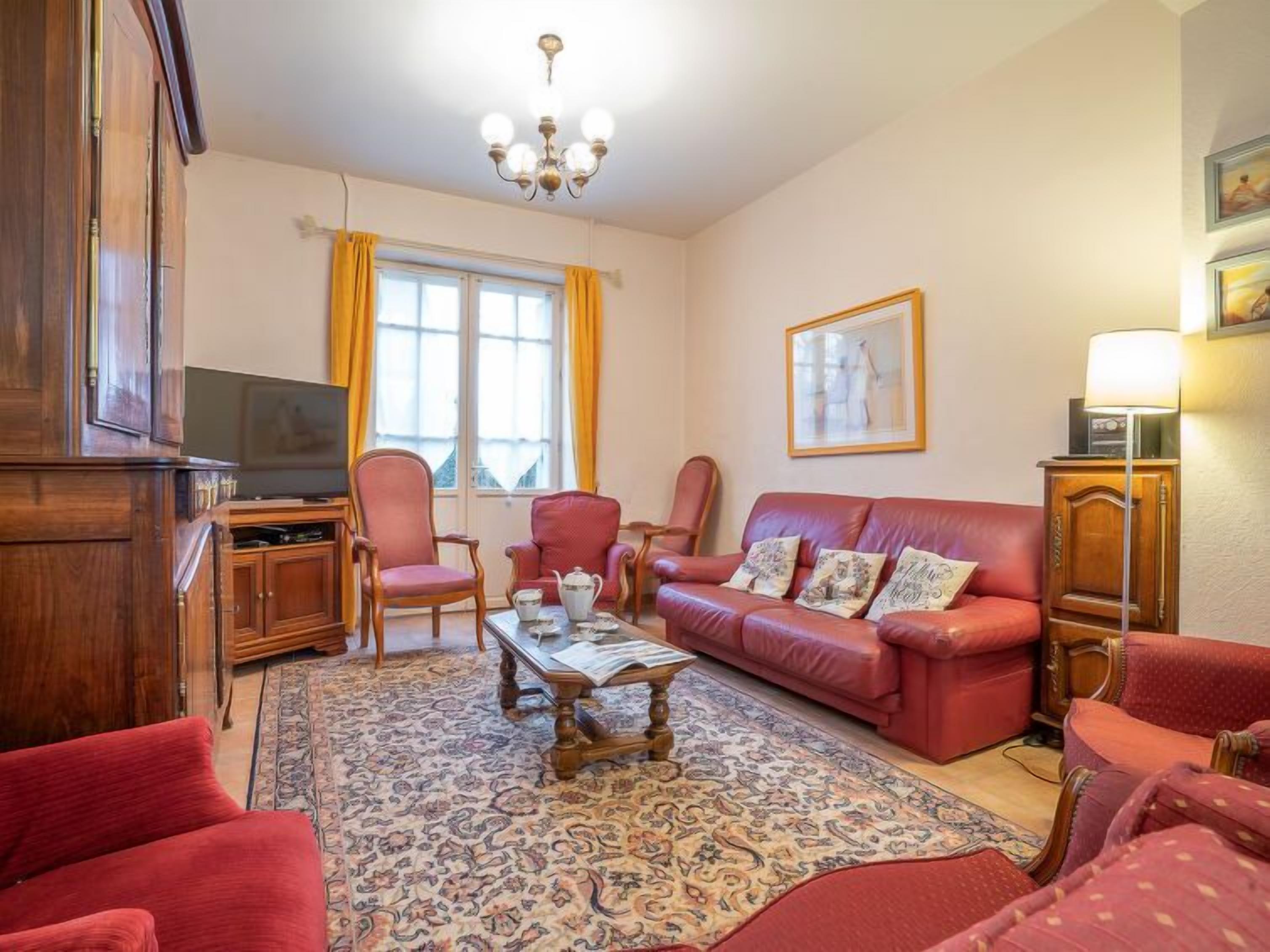 Un salon avec un canapé rouge, deux fauteuils, une table basse et un téléviseur.