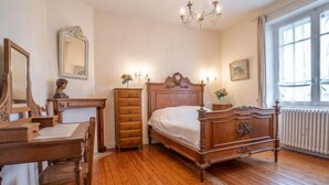 Een slaapkamer met een houten bed, een dressoir, een bureau met stoel, een spiegel en een raam met gordijnen.
