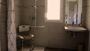 Ein Badezimmer mit Dusche, einer behindertengerechten Toilette mit Sitzgelegenheit, einem Waschbecken und einem Fenster.