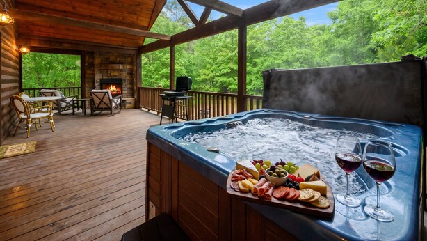 Una terraza de madera con un jacuzzi, mobiliario exterior y una chimenea de piedra.