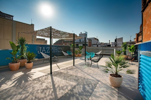 A rooftop terrace with potted plants, outdoor seating, and a clear blue sky.
