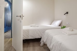 A hotel room with two beds, a door leading to a hallway, and a small plant on the wall.