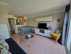 A compact living space with a kitchenette, a dining area, a sofa, a TV, and a window with curtains.