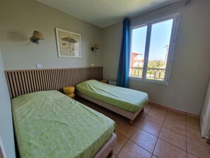 Une chambre avec deux lits, une fenêtre donnant sur un beau paysage, une lampe fixée au mur et un tableau encadré.