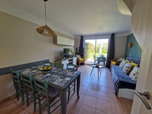 A dining area with a table and chairs, a sofa, a television, and a view of the outdoors.
