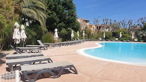 A pool area with sun loungers and umbrellas, surrounded by trees and buildings.