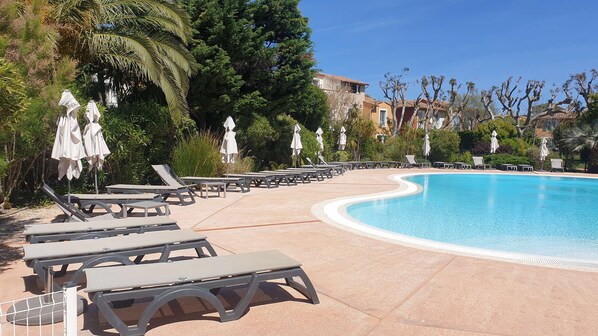 A pool area with sun loungers and umbrellas, surrounded by trees and buildings.