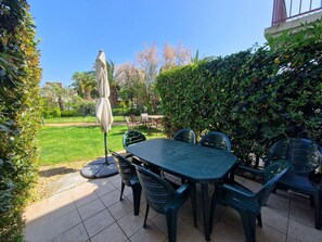 An outdoor patio with a table and chairs, surrounded by greenery and a clear sky.