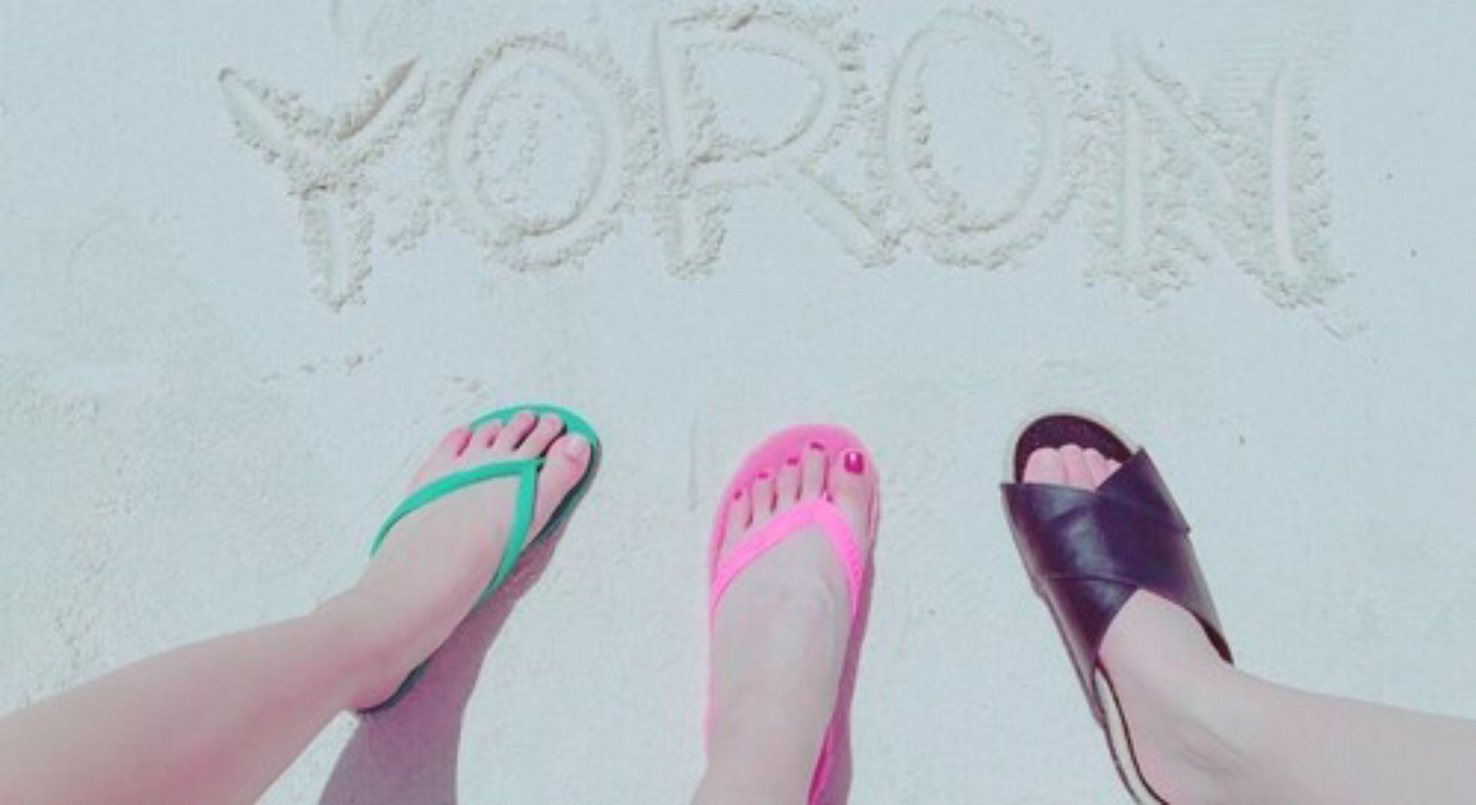 Three pairs of feet standing on sand with the word "YORONI" written in the sand.